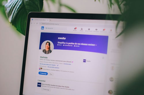 Smartphone mit Facebook-App neben einem geöffneten Laptop auf einem Holztisch.